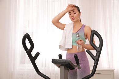 Photo of Tired woman after training on modern elliptical machine at home