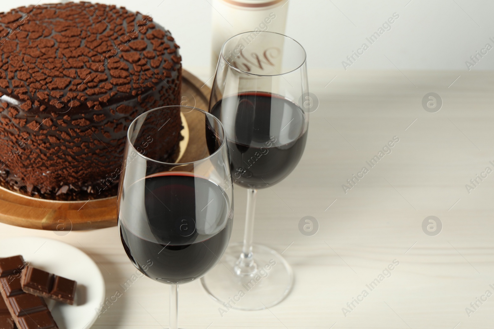 Photo of Delicious truffle cake, chocolate pieces and red wine on light wooden table, space for text