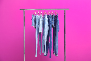 Rack with stylish jeans and denim shorts on color background