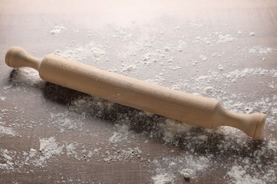 Photo of Rolling pin and scattered flour on wooden table, closeup