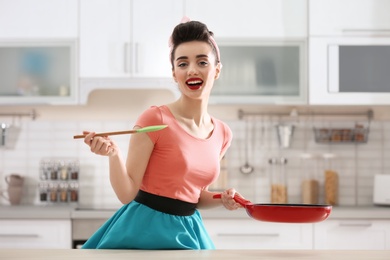 Photo of Funny young housewife with spoon and frying pan in kitchen