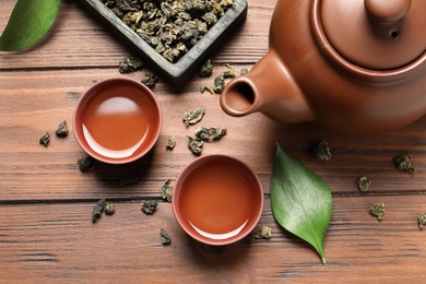 Photo of Cups and teapot of Tie Guan Yin oolong on wooden background, flat lay