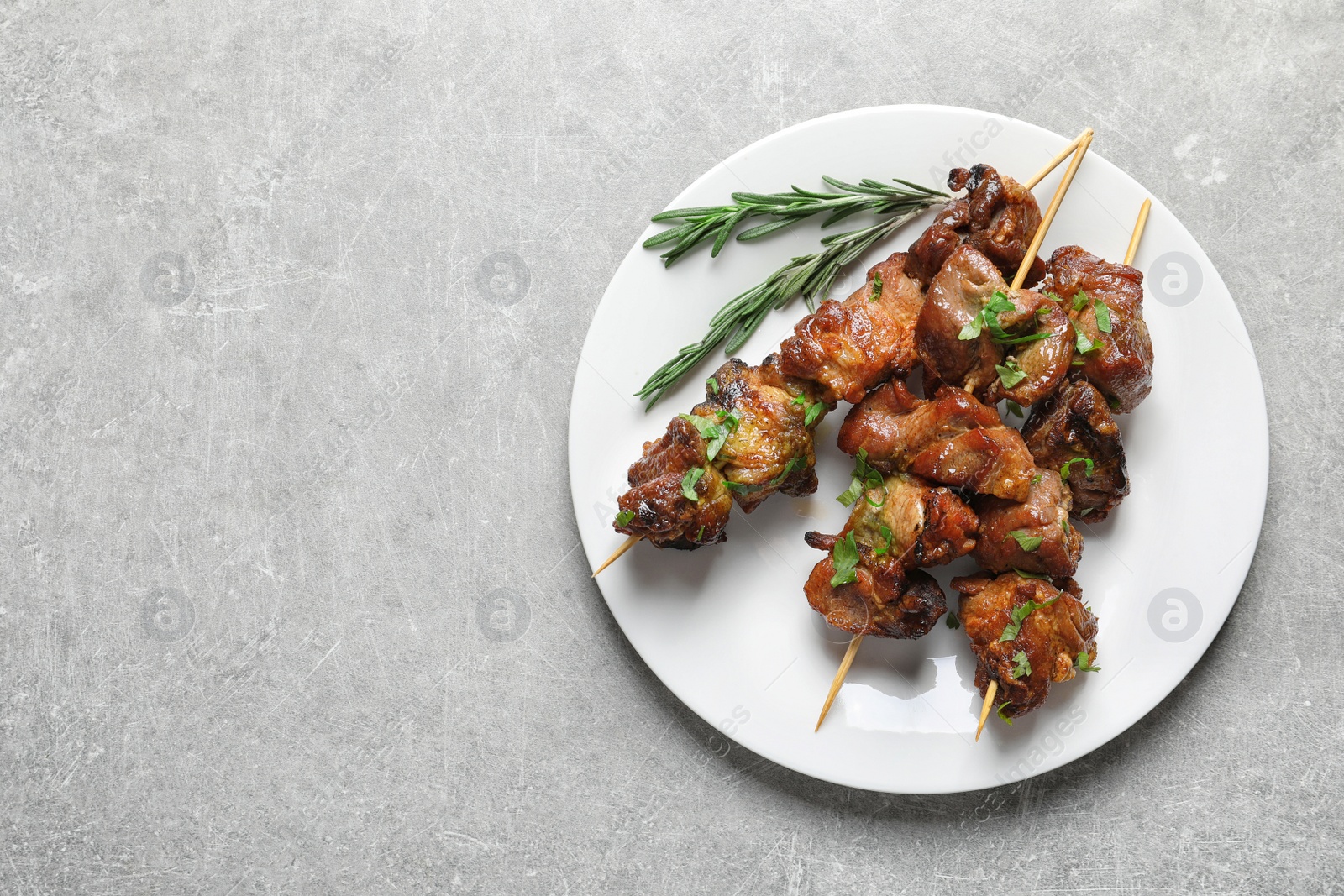 Photo of Plate of delicious barbecued meat served on gray table. Space for text