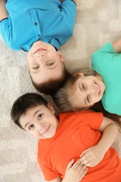 Photo of Cute little children lying together on floor in playing room, top view