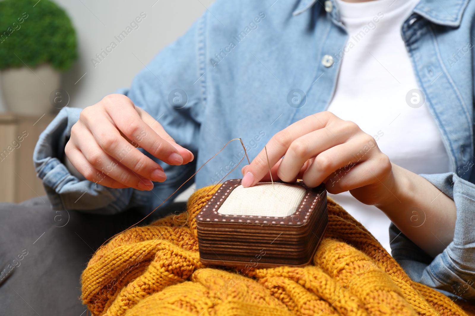 Photo of Woman taking needle out of pin cushion indoors, closeup