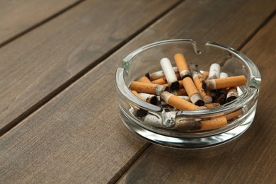 Photo of Glass ashtray with cigarette stubs on wooden table. Space for text
