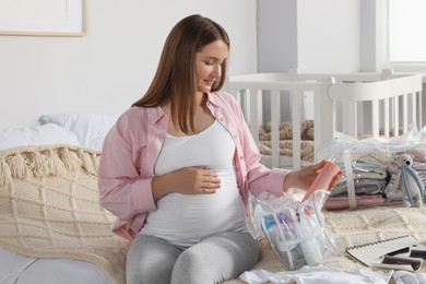Pregnant woman packing baby stuff to bring into maternity hospital in bedroom