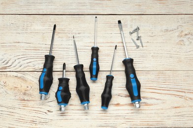 Photo of Set of screwdrivers and screws on wooden table, flat lay