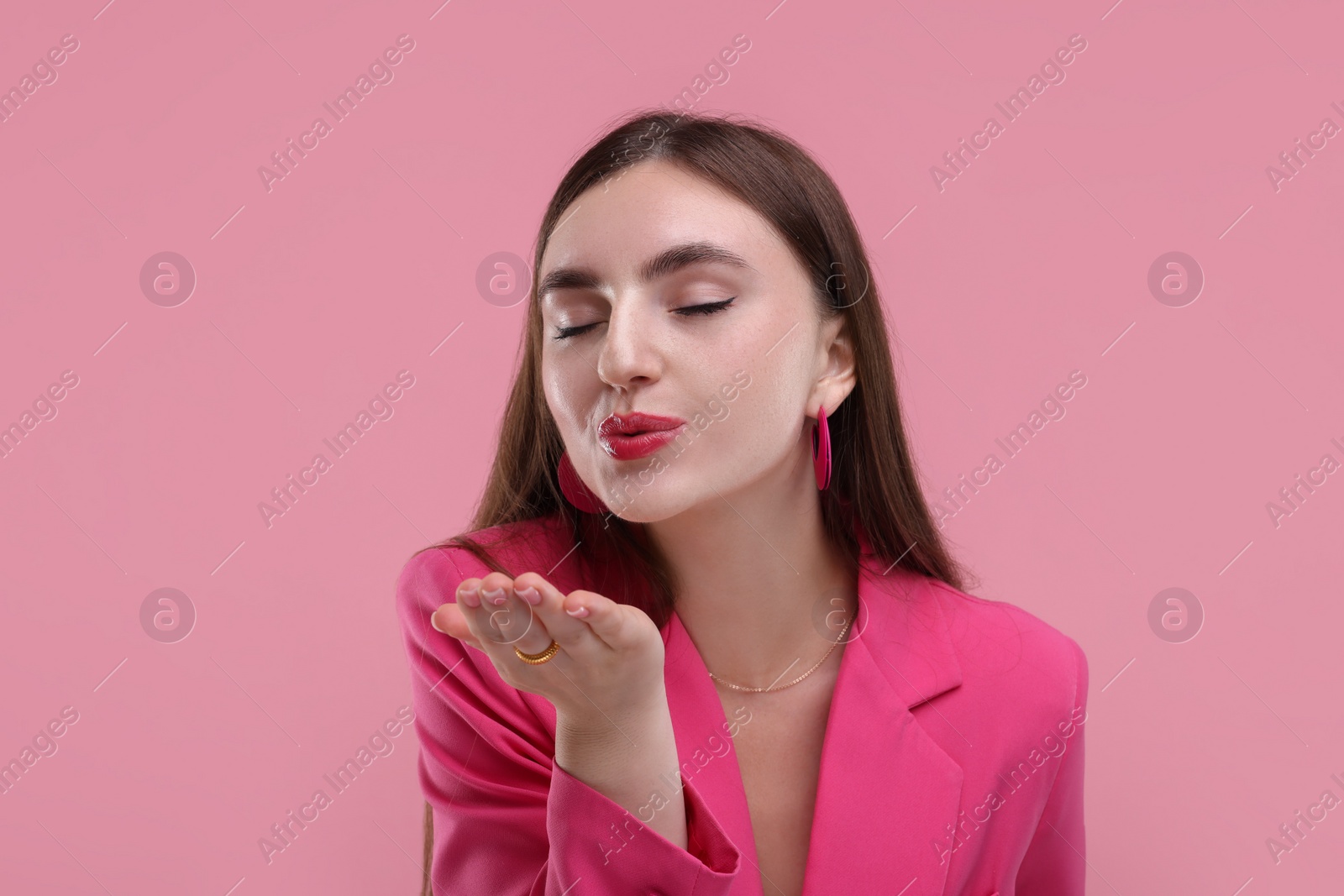 Photo of Beautiful woman in pink clothes blowing kiss on color background