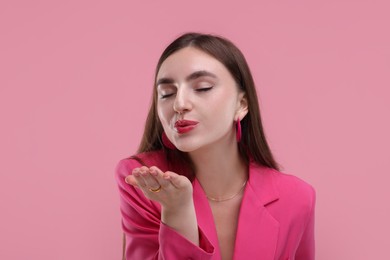 Photo of Beautiful woman in pink clothes blowing kiss on color background
