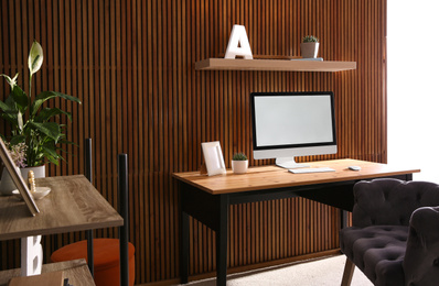 Photo of Comfortable workplace with computer near wooden wall in stylish room interior. Home office design