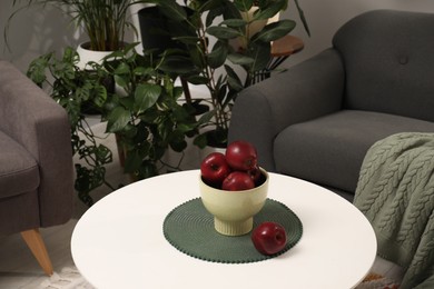 Photo of Red apples on coffee table near sofa and houseplants in room