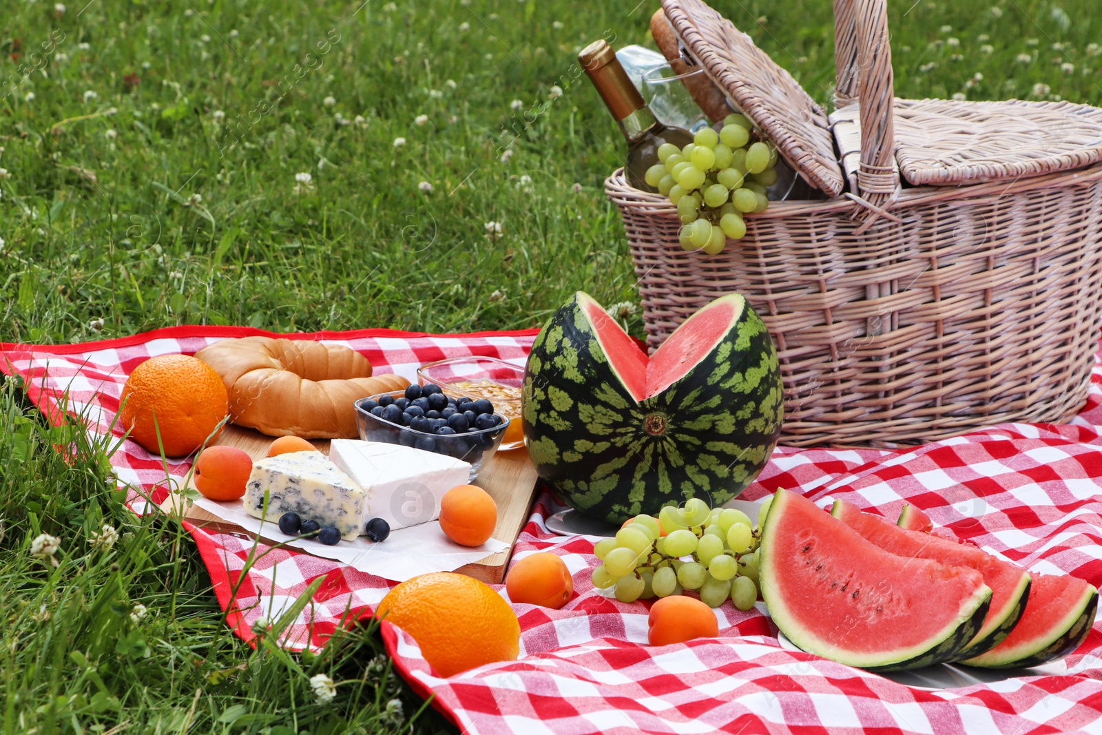 Photo of Picnic blanket with delicious food and wine outdoors on summer day