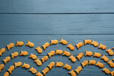 Photo of Delicious fish shaped crackers on blue wooden table, flat lay. Space for text