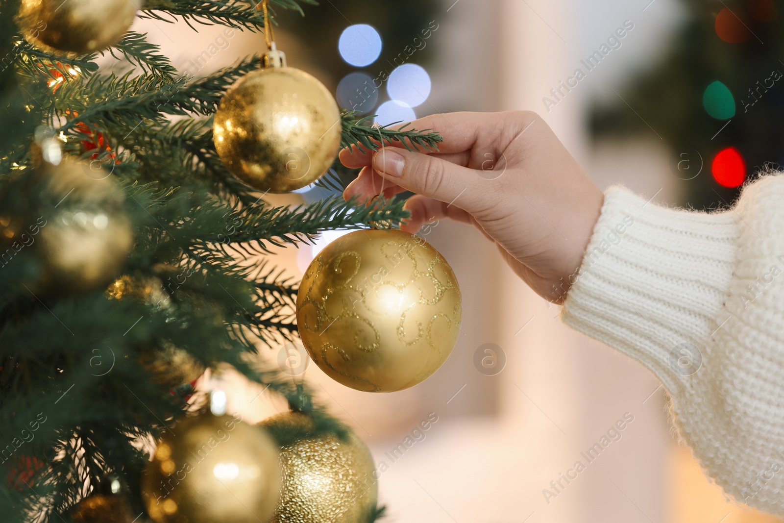 Photo of Woman decorating Christmas tree with golden festive ball on light background, closeup