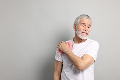 Image of Senior man suffering from pain in shoulder on grey background. Space for text