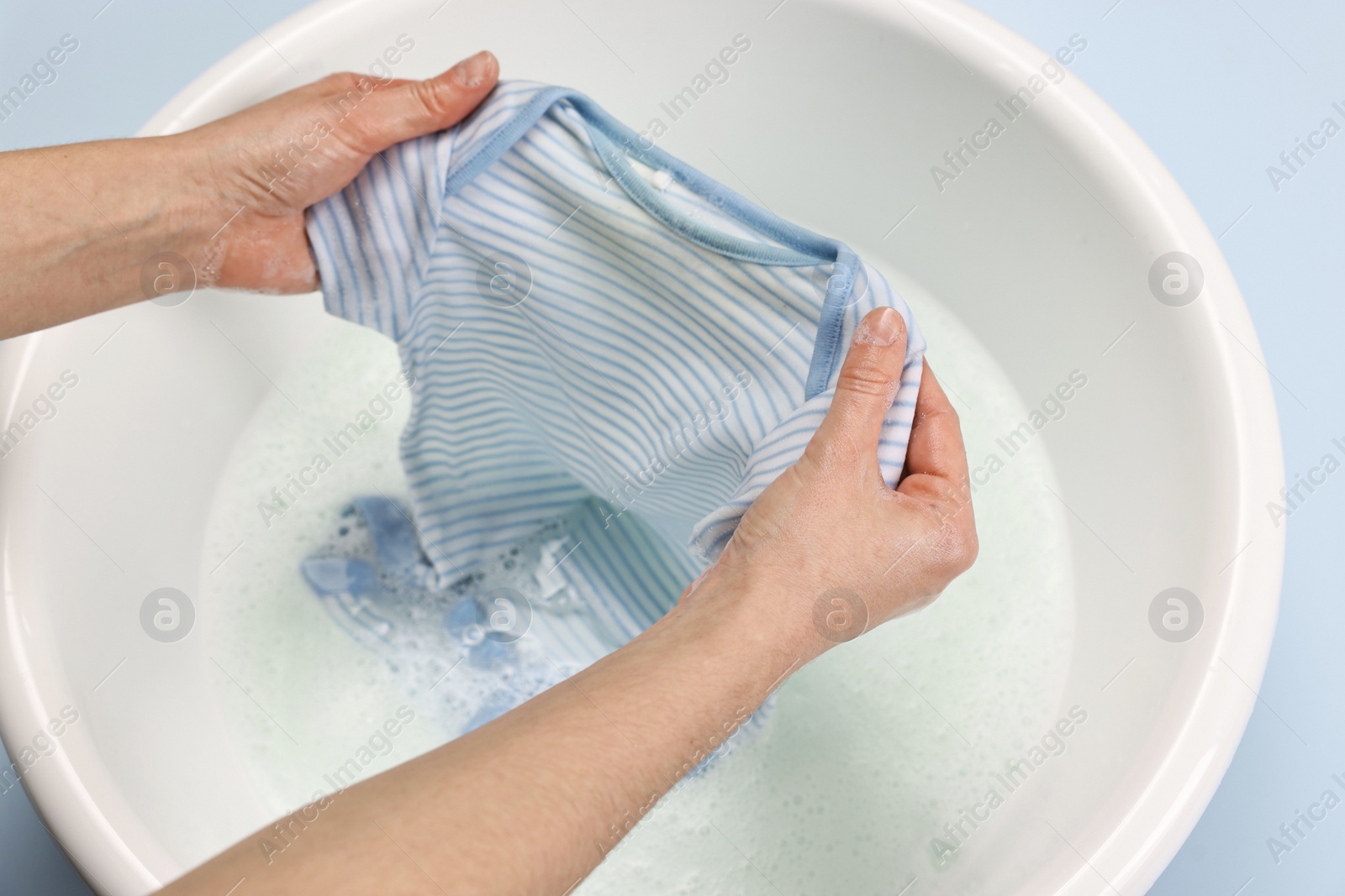 Photo of Woman washing baby clothes in basin on light blue background, closeup