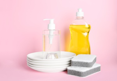 Detergents, plates and sponges on pink background. Clean dishes