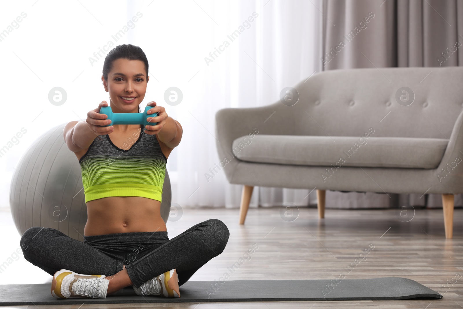 Photo of Young woman in fitness clothes doing exercise with dumbbell at home. Space for text