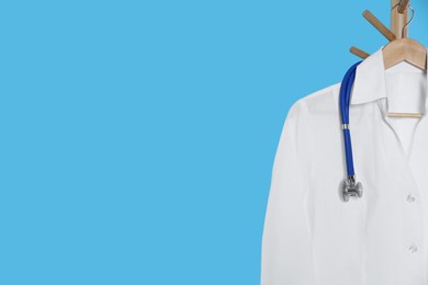 Photo of White medical uniform and stethoscope hanging on rack against light blue background. Space for text