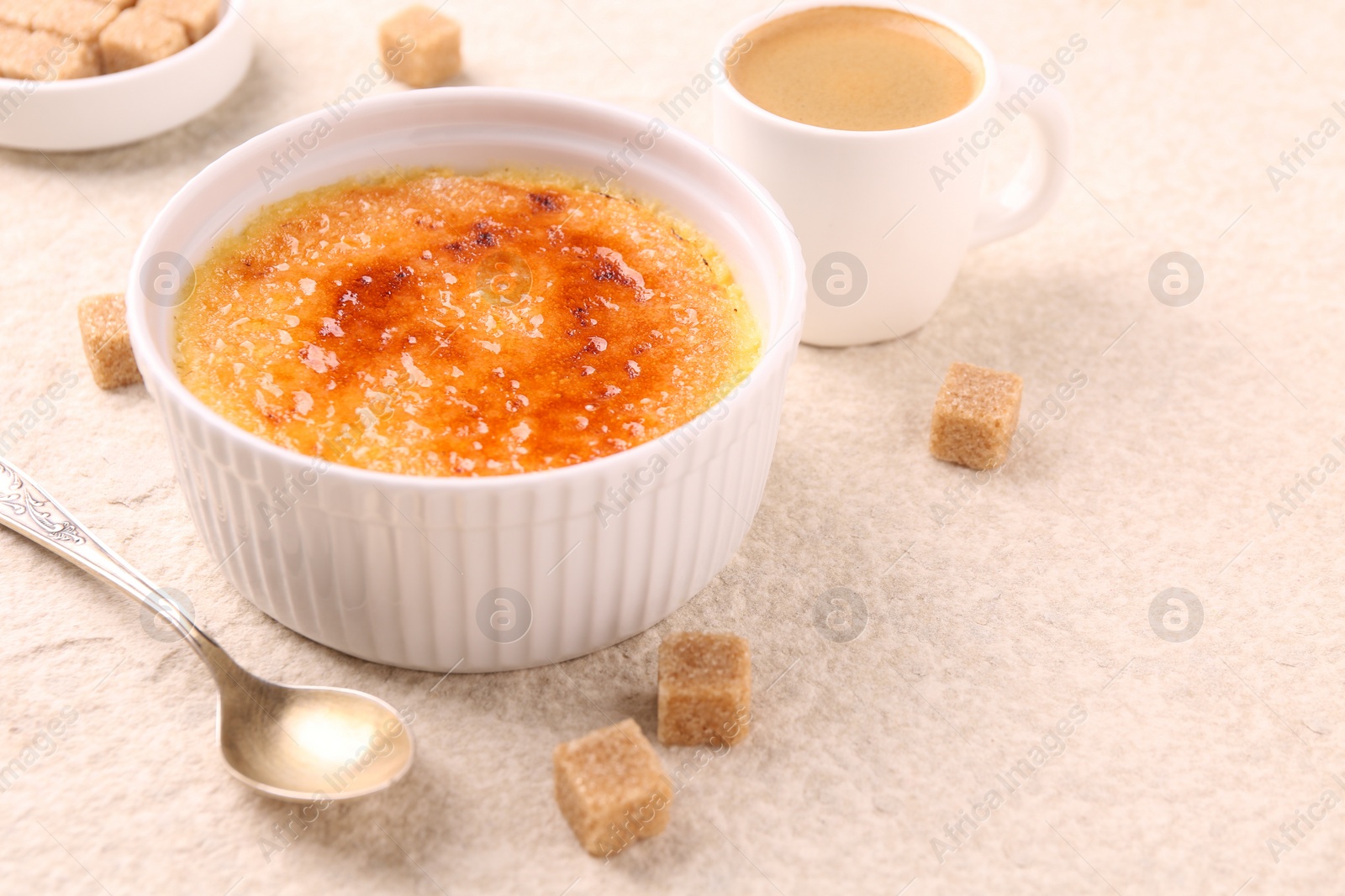 Photo of Delicious creme brulee in bowl, sugar cubes, coffee and spoon on light textured table, closeup. Space for text