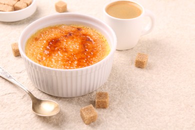 Photo of Delicious creme brulee in bowl, sugar cubes, coffee and spoon on light textured table, closeup. Space for text