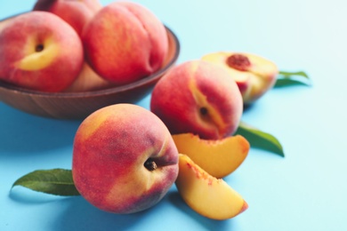 Photo of Fresh ripe peaches and green leaves on light blue background, closeup