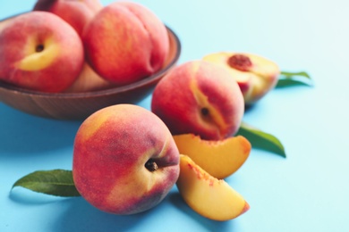 Fresh ripe peaches and green leaves on light blue background, closeup