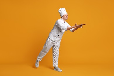 Photo of Portrait of happy confectioner in uniform holding cake stand on orange background