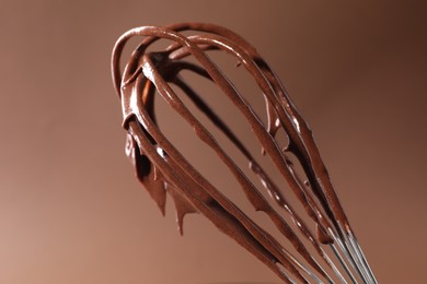 Photo of Chocolate cream flowing from whisk on brown background, closeup