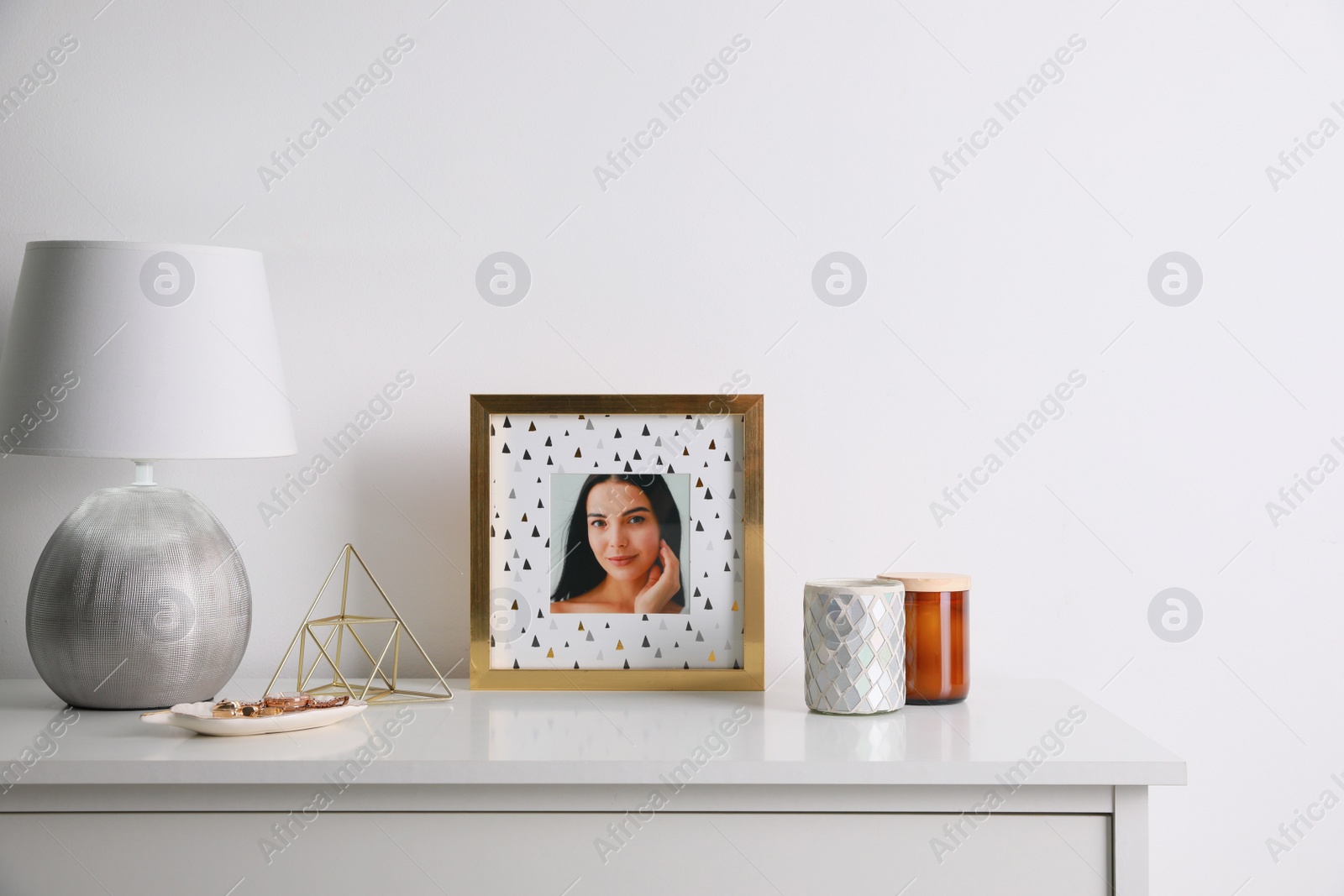 Photo of Photo frame with portrait of beautiful young woman near stylish decor on white table. Space for text