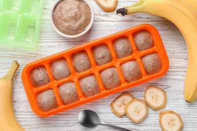 Photo of Banana puree in ice cube tray with ingredients on white wooden table, flat lay