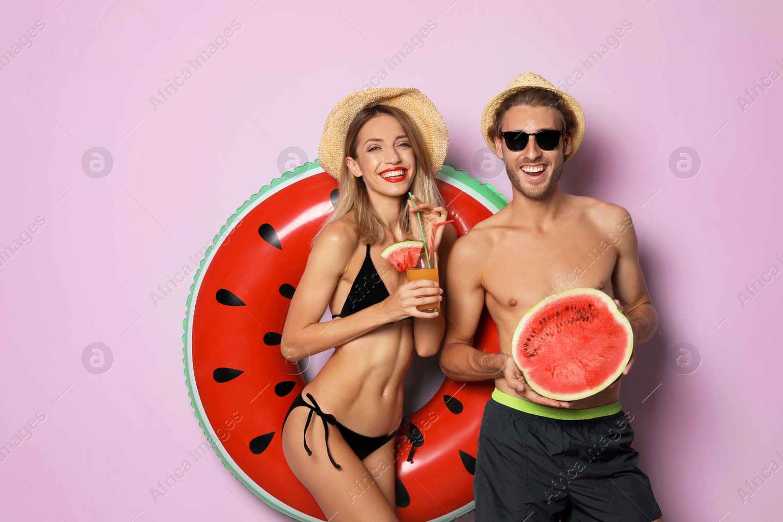 Photo of Happy young couple in beachwear with inflatable ring and cocktail on color background