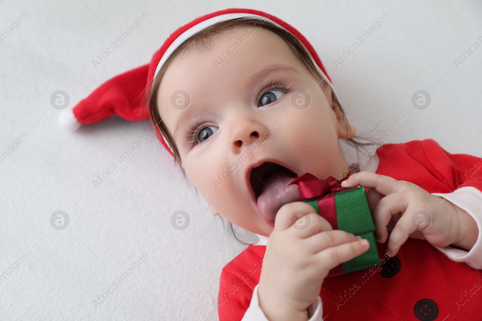 Photo of Cute baby wearing festive Christmas costume with gift box in crib, closeup