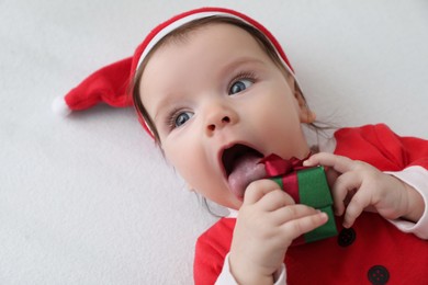 Photo of Cute baby wearing festive Christmas costume with gift box in crib, closeup