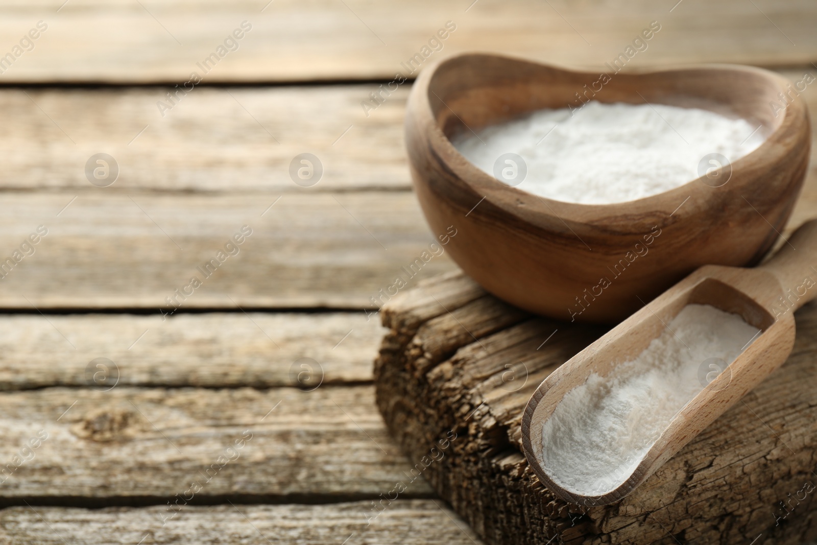 Photo of Baking powder in bowl and scoop on wooden table, closeup. Space for text