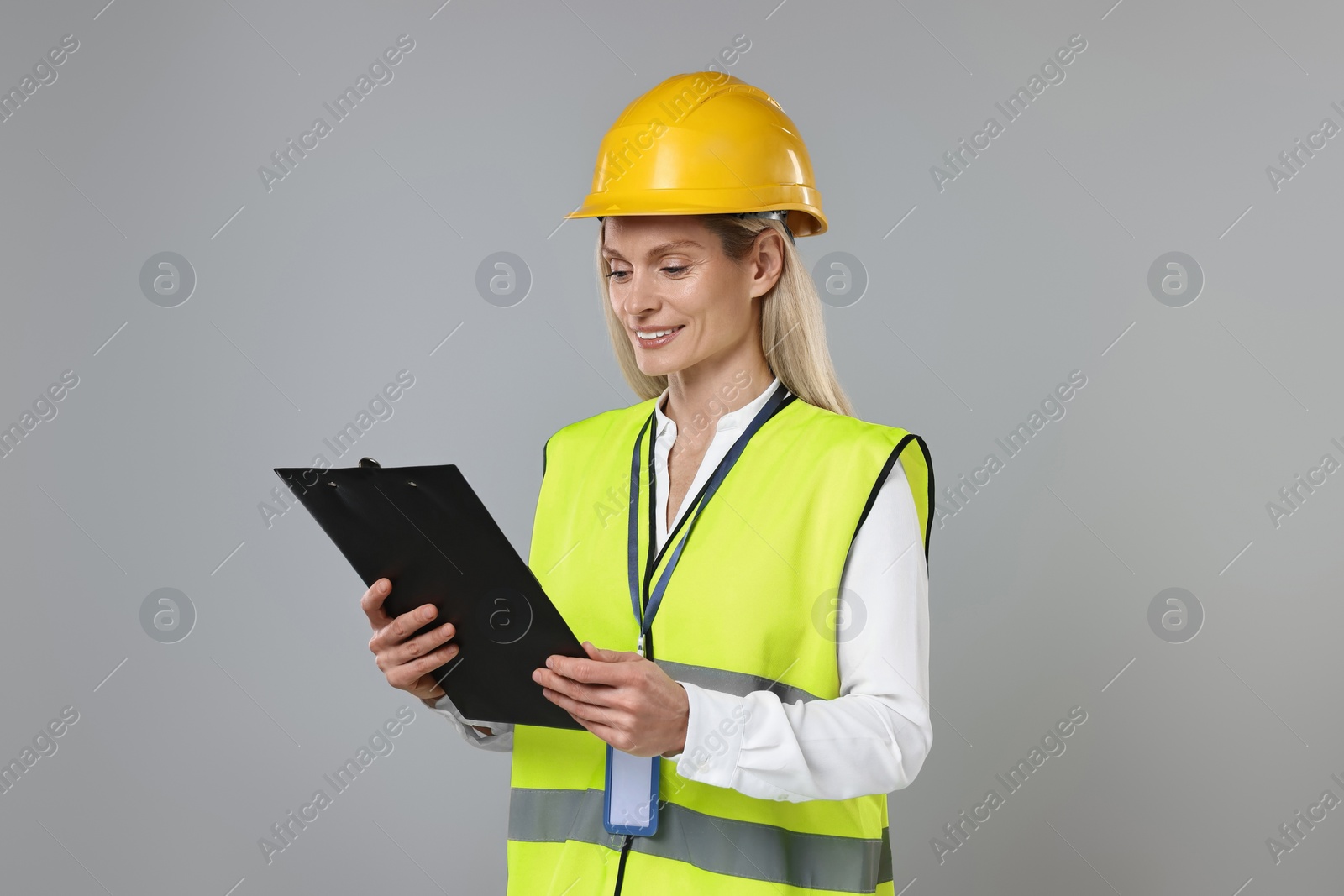 Photo of Engineer in hard hat holding clipboard on grey background