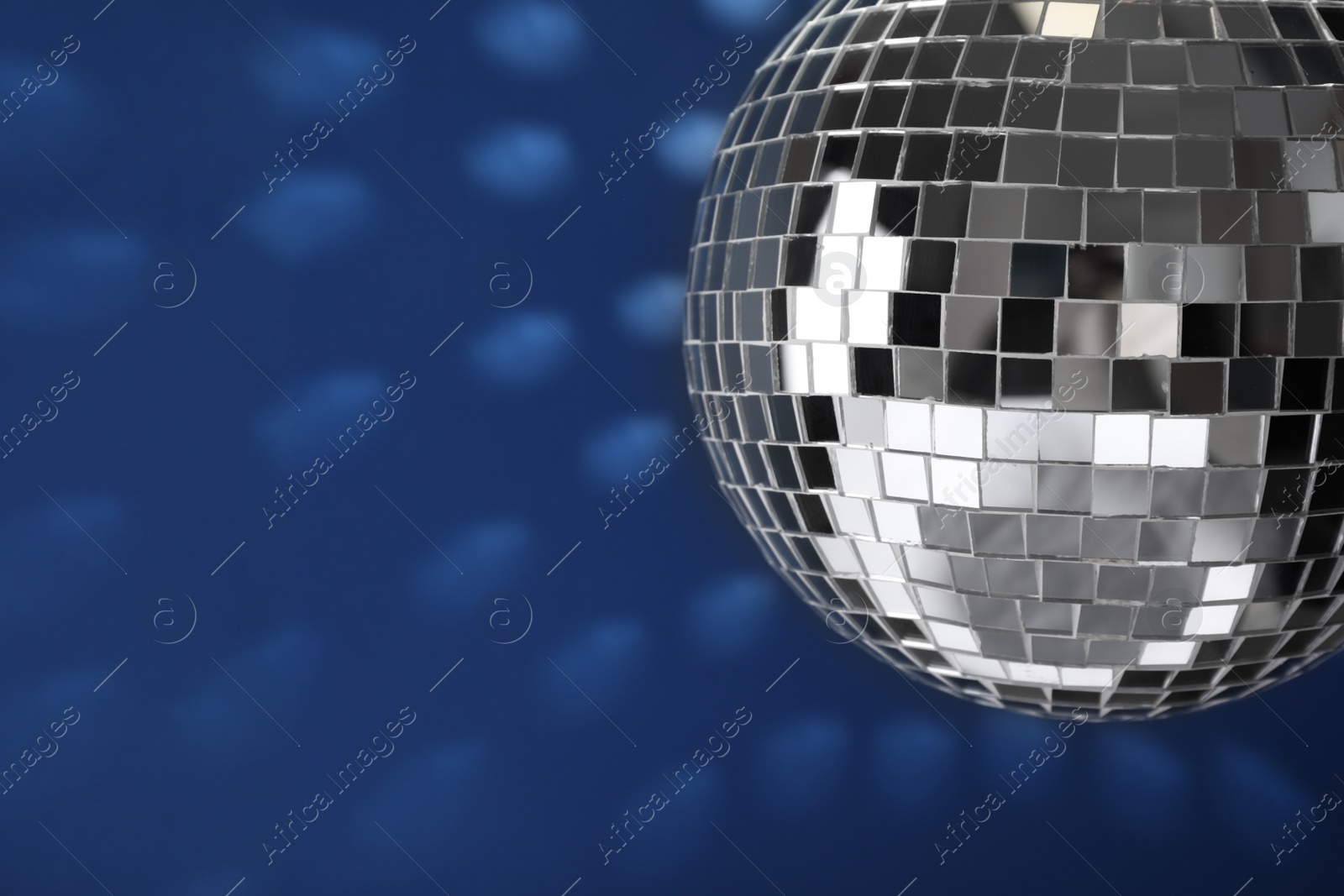 Photo of Shiny disco ball on blue background, closeup. Space for text