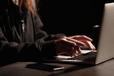 Woman using laptop at table in darkness, closeup. Loneliness concept