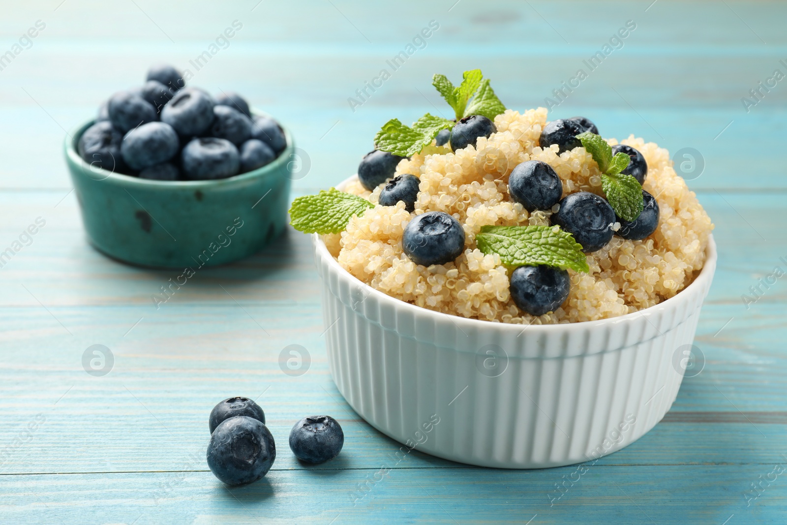 Photo of Tasty quinoa porridge with blueberries and mint in bowl on light blue wooden table