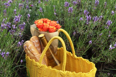 Photo of Yellow wicker bag with beautiful roses, bottle of wine and baguettes in lavender field