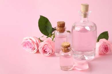 Bottles of essential oil and roses on pink background