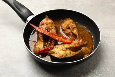 Tasty fish curry in frying pan on light grey table, closeup. Indian cuisine