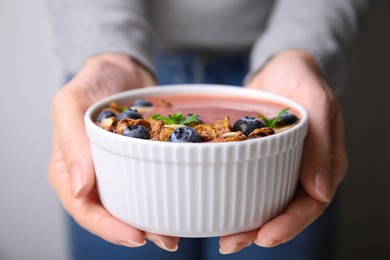 Woman holding bowl of delicious fruit smoothie with fresh blueberries and granola against blurred background, closeup