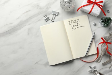 Photo of Inscription 2022 Goals written in planner and Christmas decor on white marble background, flat lay. New Year aims