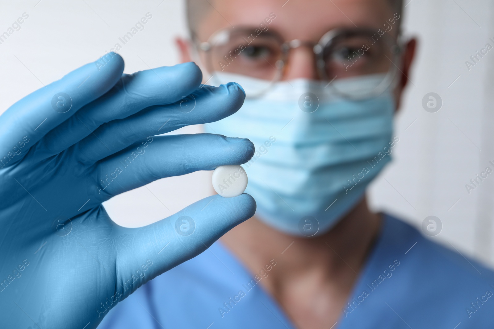 Photo of Doctor holding pill on light background, selective focus. Space for text