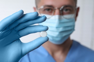 Photo of Doctor holding pill on light background, selective focus. Space for text