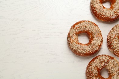 Photo of Delicious fresh bagels with sesame seeds on white wooden table, flat lay. Space for text