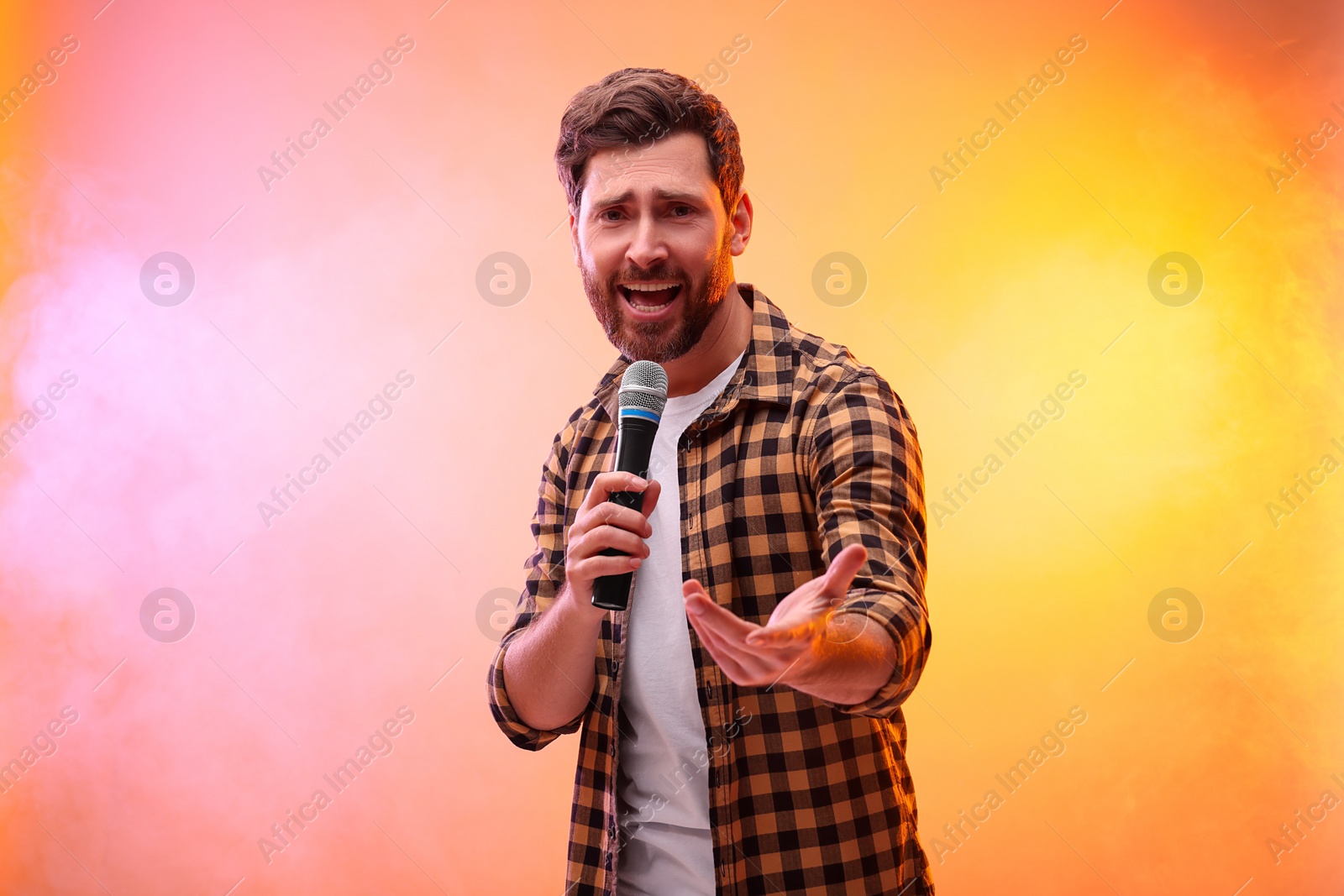 Photo of Handsome man with microphone singing in color lights