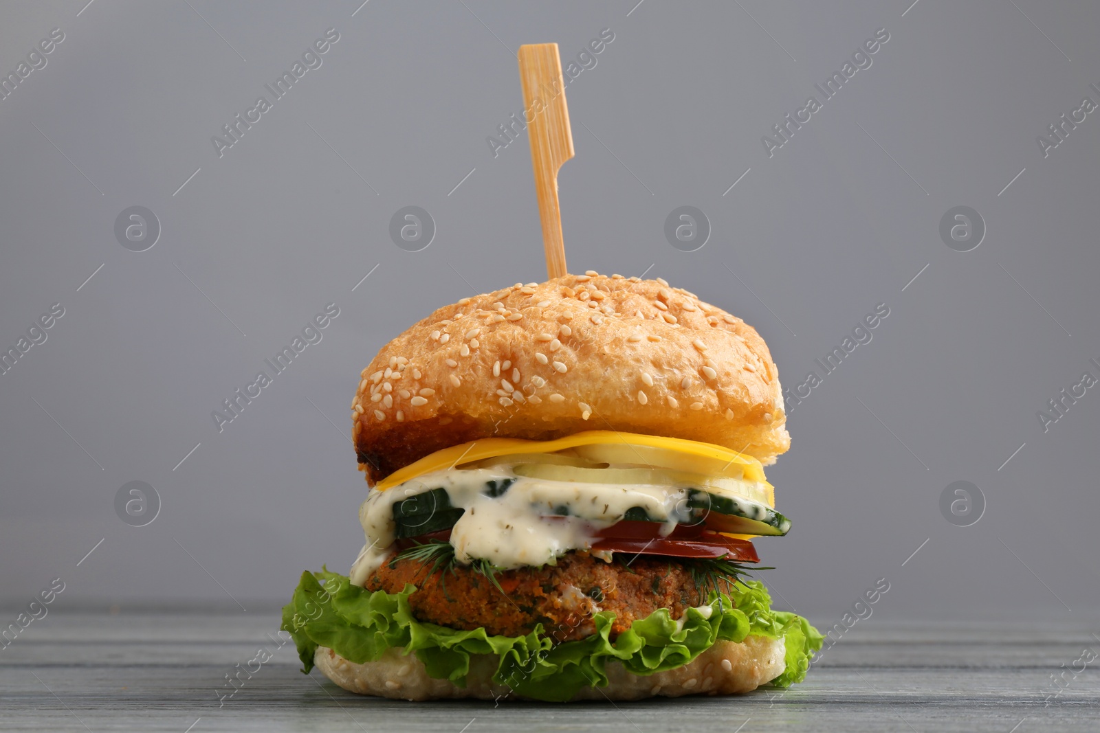 Photo of Delicious vegetarian burger on grey wooden table